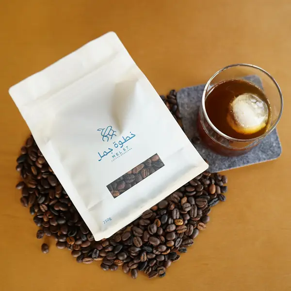 Pose un sachet de café plat sur des grains de café torréfiés à côté du café glacé pour la présentation du produit