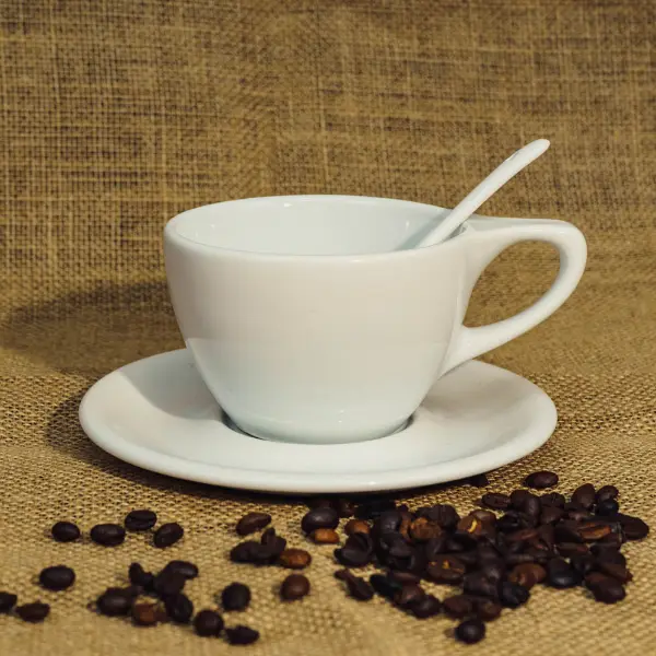 Tasse à café en céramique blanche à couvercle plat avec poignée exposée avec des grains de café